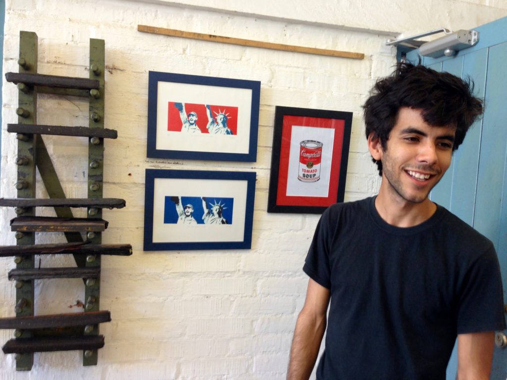 A 20-something artist stands in front of three small prints.