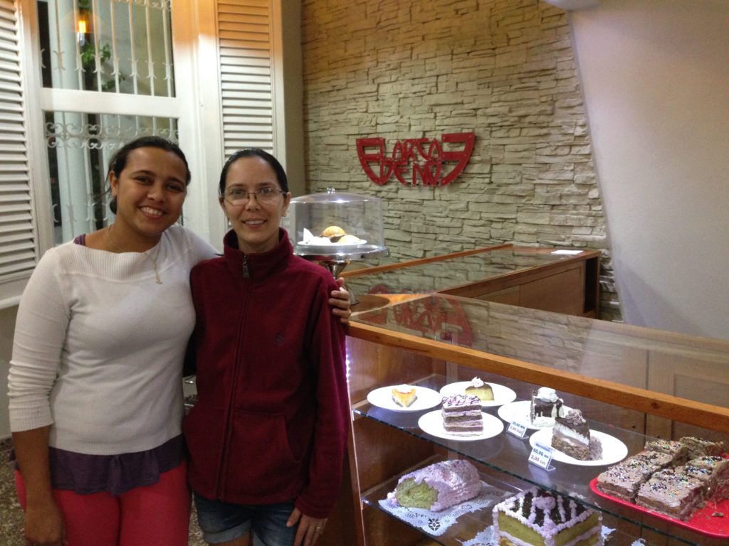 Two women pose for a photo in front of a display case of baked goods