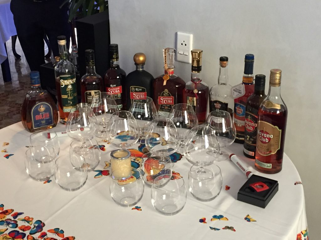A row of rum bottles sit on a white tablecloth. In front of them are about a dozen glasses.