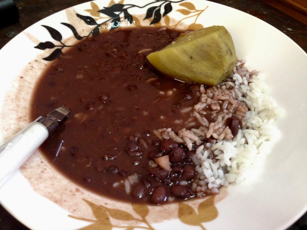 A bowl of beans and rice with a slice of yellow sweet potato and a spoon