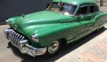 A green classic car sits parked at a curb