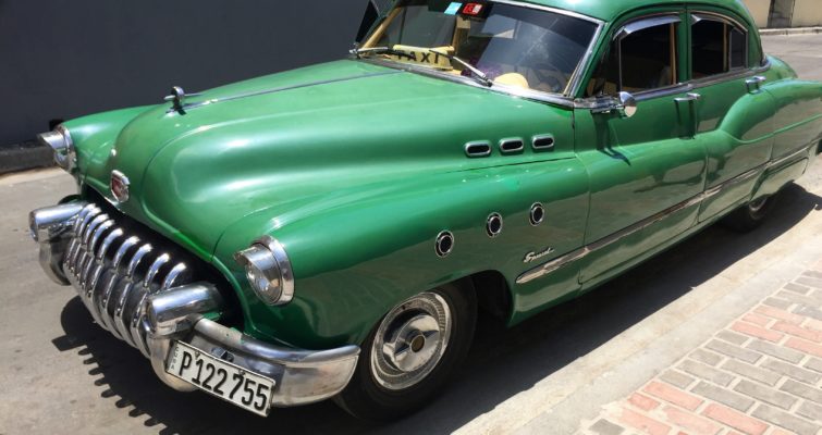 A green classic car sits parked at a curb