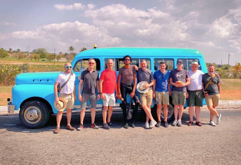A group of eight men stand in front of a bright aqua vintage van